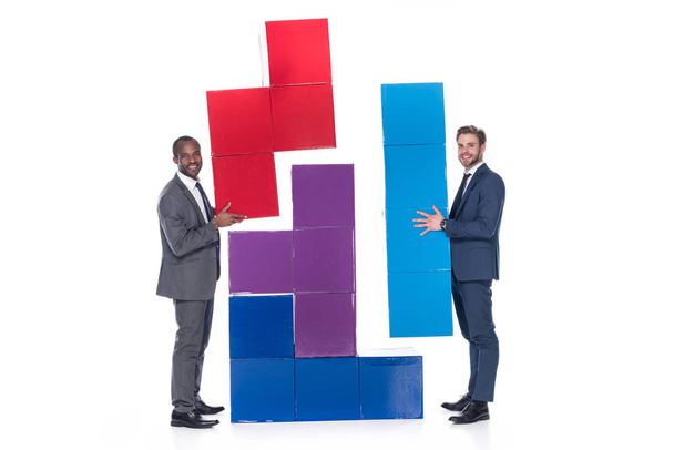 Seitenansicht von lächelnden multiethnischen Geschäftsleuten mit bunten Blöcken isoliert auf weißem, Teamwork-Konzept - Foto, Bild