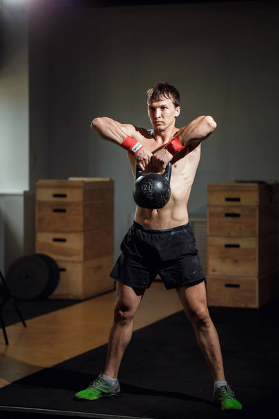 Intenzivního výcviku. muž v oblečení cvičit s konvicí bell v tělocvičně - Fotografie, Obrázek