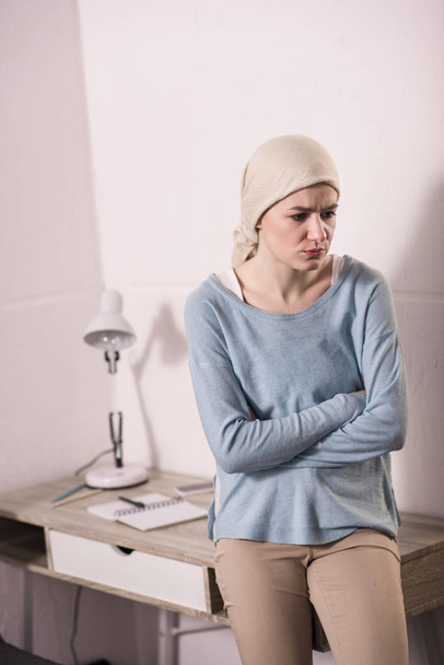 upset sick young woman in kerchief sitting on table and looking away  - Photo, Image