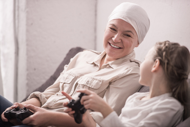 happy grandmother and granddaughter playing with joysticks, cancer concept   - Photo, Image