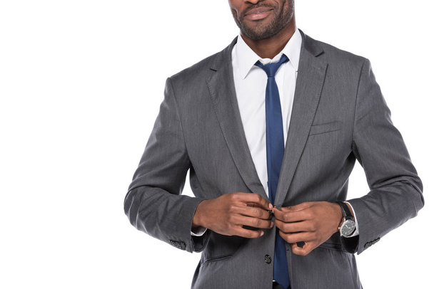abgeschnittene Aufnahme eines afrikanisch-amerikanischen Geschäftsmannes, der Anzug auf Weiß knöpft - Foto, Bild
