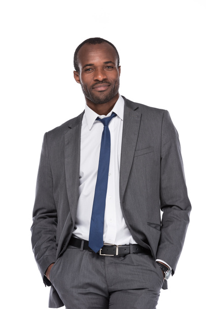 smiling african american businessman in suit with hands in pockets  isolated on white - Photo, image