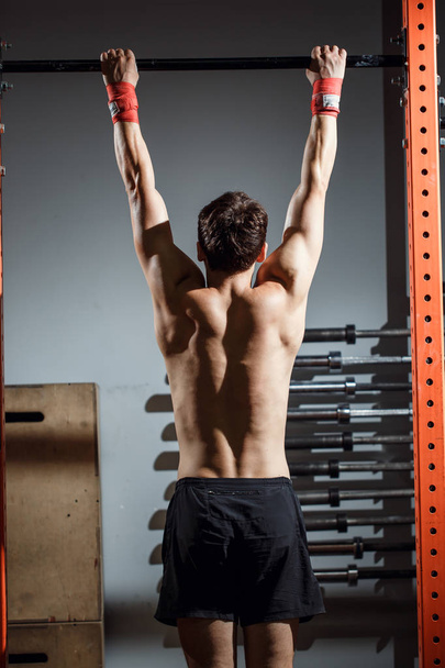 atractivo jóvenes adultos masculinos haciendo pull ups en la barra en el gimnasio de entrenamiento de cross fit
 - Foto, imagen