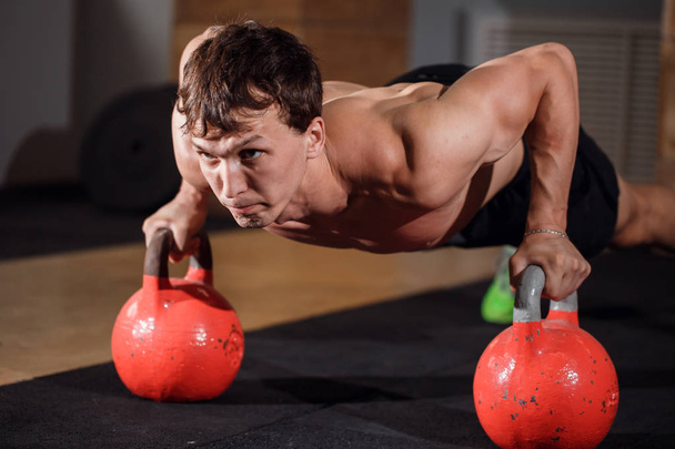 Gym man push-up strength pushup exercise with Kettlebell in a workout - Fotó, kép