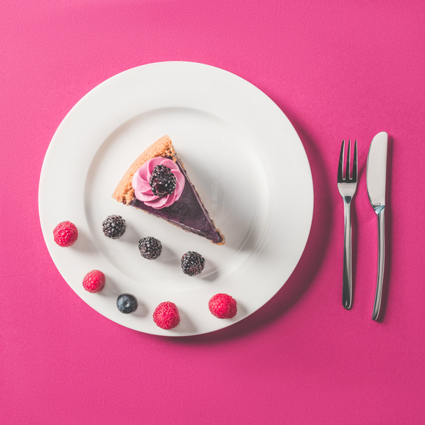 top view of piece of cake with berries on plate on pink surface - Photo, Image