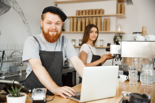 Coffee Business Concept - Jeune barman barbu beau, barista ou gestionnaire de travail et de rabotage dans un ordinateur portable au café moderne
. - Photo, image