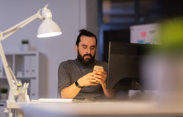 creative man with smartphone at night office - Foto, Bild
