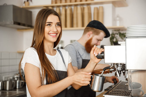 Coffee Business Concept - muotokuva lady barista esiliina valmistelee ja höyryssä maitoa kahvin tilauksen kumppaninsa seistessä kahvilassa
. - Valokuva, kuva