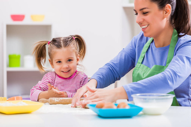 Happy mother and daughter are making cookies in their kitchen. - Photo, Image