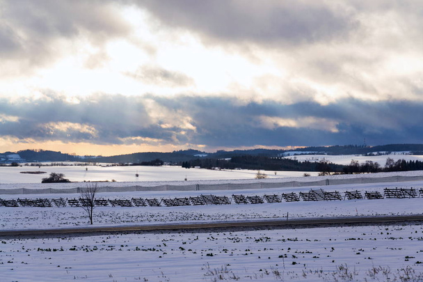Barreiras de neve de madeira e plástico perto da estrada na paisagem nevada durante o pôr do sol, tráfego pendular previsão meteorológica conceito de notícias
 - Foto, Imagem