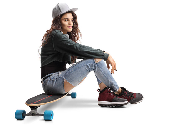 Teenage skater girl sitting on a longboard isolated on white background - Foto, afbeelding