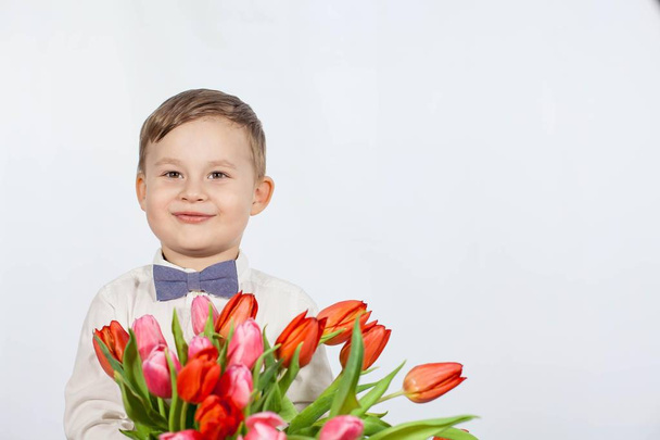 Cute little boy holding a bouquet of flowers. Tulips. Mothers Day. International Womens Day. Portrait of a happy little boy on - Photo, Image