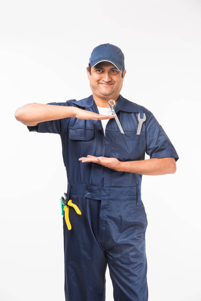 Индийский счастливый автомеханик в синем костюме и кепке держит гаечный ключ инструмент в действии, изолированные на белом фоне
 - Фото, изображение