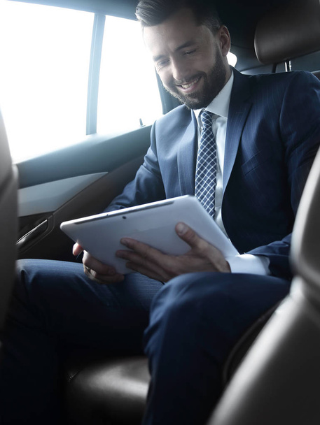 businessman with a digital tablet sitting in the back seat of a car - Foto, Imagen