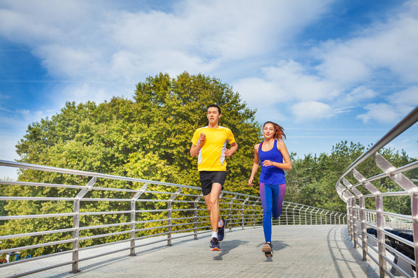 Sporty young man and woman running across a bridge during morning run in summer - Photo, Image