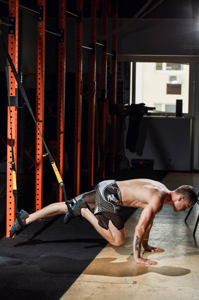 Using TRX bands, doing push-ups and torso rotations with legs suspended. - Foto, imagen
