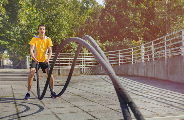 Sportsman making wave movement with battle ropes during crossfit workout outdoors - Photo, Image
