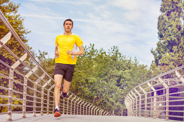 Young guy running across the bridge at park, fitness and health care concept - Φωτογραφία, εικόνα