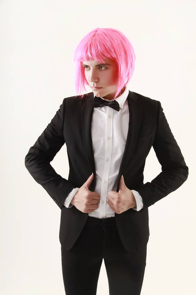 chico joven elegante y divertido de pie en traje de negocios y peluca de las mujeres de color rosa sobre fondo blanco solo
 - Foto, Imagen