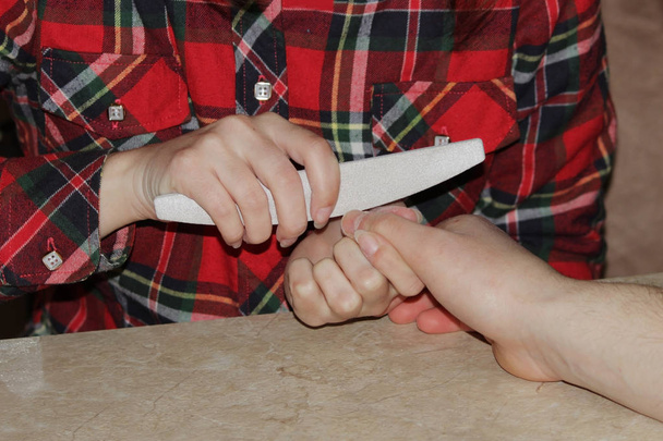 Φοιτητής στο εκπαιδευτικά σεμινάρια μανικιούρ δίνει σχήμα για τα νύχια το χέρι ενός άνδρα πελάτη με ένα πριόνι από στιλβωμένο - Φωτογραφία, εικόνα