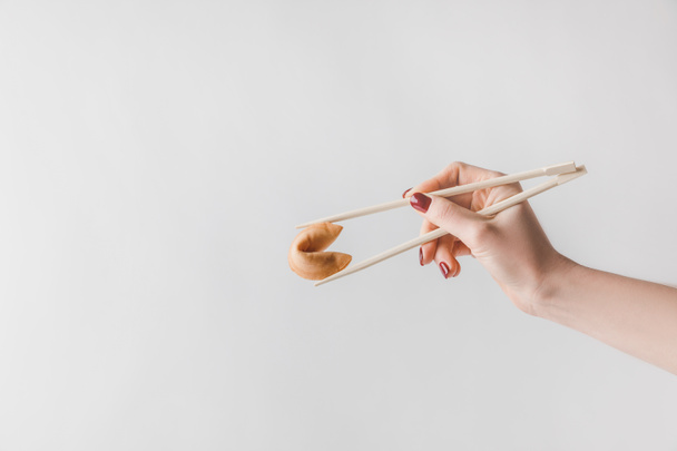 白で隔離の箸を使って中国語のフォーチュン クッキーを保持している女性のトリミングされた画像 - 写真・画像