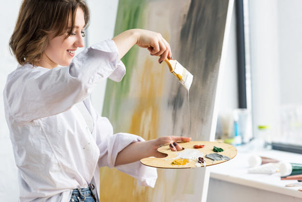 Young girl holding brush and palette in light studio - Foto, Bild