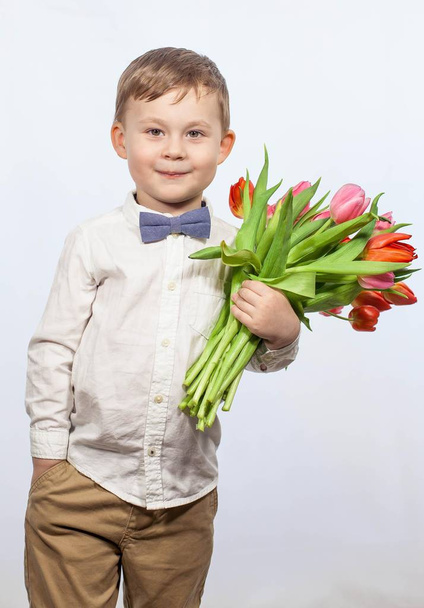 Милый мальчик с букетом цветов. Тюльпаны. День Матери. Международный женский день. Портрет счастливого мальчика на
 - Фото, изображение