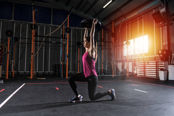 Решительная спортсменка, тренирующаяся в тренажерном зале с диском для штанги
 - Фото, изображение