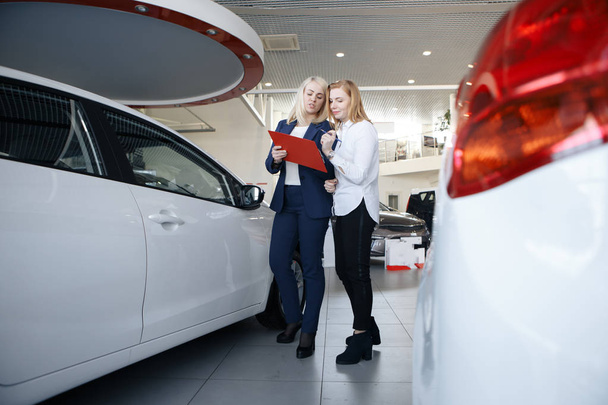 Two woman signing a deal to purchase a car with the saleslady leaning through the open window and pointing to the contract - Photo, Image