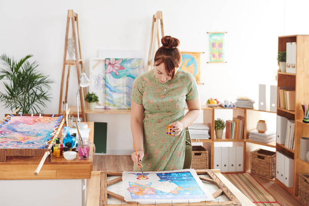 Творческая молодая женщина наслаждается живописью в своей студии
 - Фото, изображение