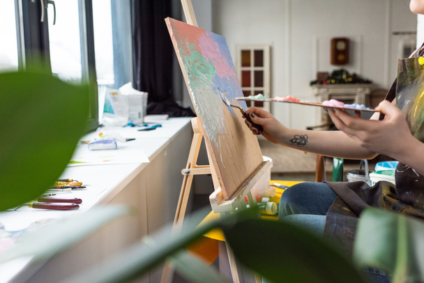 Vista de cerca de la joven chica creativa aplicando imprimación sobre lienzo en estudio de luz
 - Foto, imagen