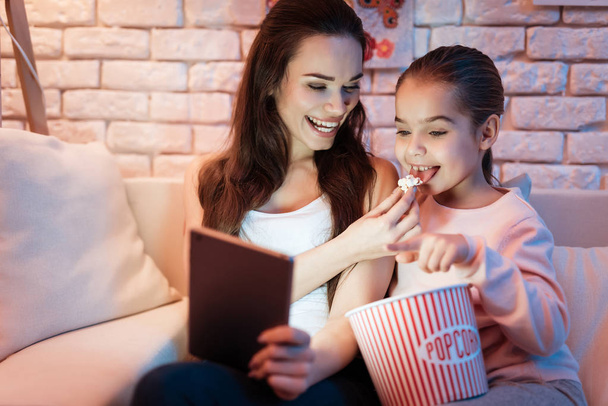 Mother and daughter watching movies on tablet eating popcorn at night at home. - Fotó, kép