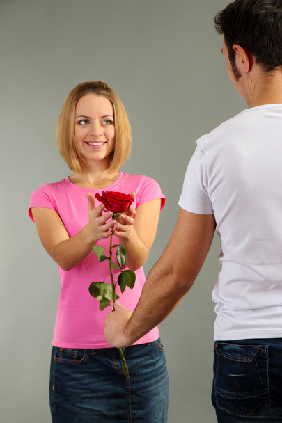 Loving man giving woman rose on grey background - Foto, imagen