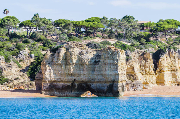 Пещера и известняковая арка. Люди идут под аркой по пляжу. Албуфейра, Алгарве, Португалия
. - Фото, изображение