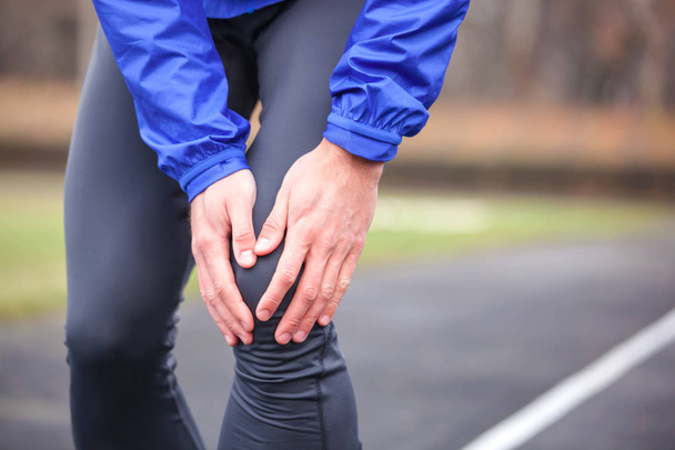 Cropped shot of a young runner holding his injured knee while ru - Foto, Bild