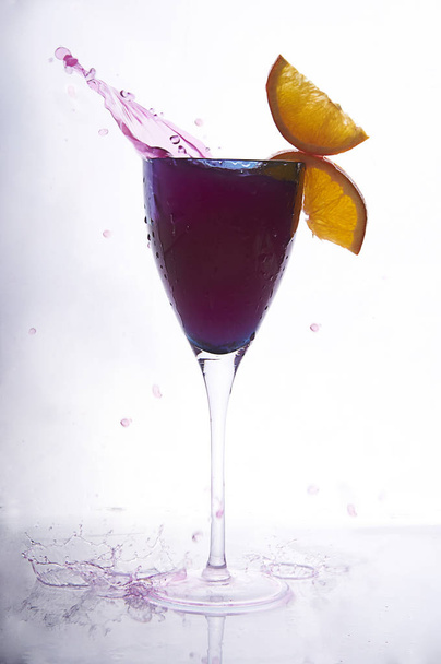 коктейль в голубом бокале, украшенном апельсинами. брызги красной жидкости в бокале вина изолированы на белом
 - Фото, изображение