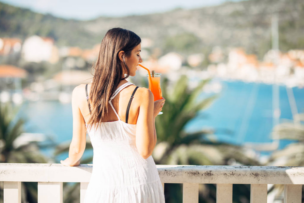 Молодая женщина наслаждается красочным коктейлем на террасе с панорамным видом на гостиницу. Холодный вкусный коктейль смузи для летнего жаркого дня. Наслаждаясь летним отдыхом.
 - Фото, изображение