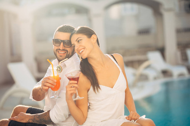 Youbg cheerful loving couple having cocktails by the pool on summer vacation.Romantic evening in luxury resort.Celebrating love ,engagement,anniversary.Enjoying time together.Relaxing with your better half - Foto, Bild