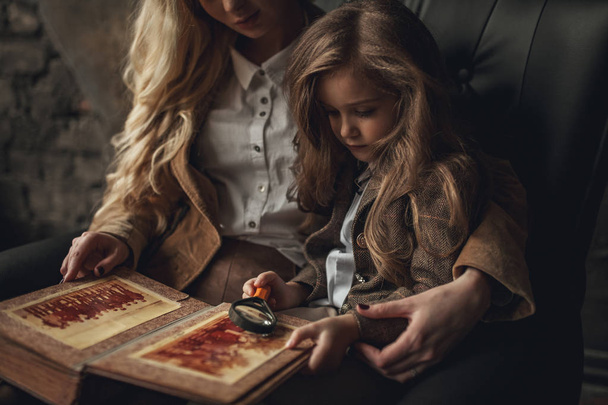 Lapsi tyttö naisen kuva Sherlock Holmes istuu ja näyttää valokuva-albumi suurennuslasi taustalla vanha sisustus
. - Valokuva, kuva