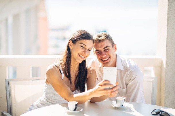 Attractive couple having first date.Coffee with a friend.Smiling happy people making a selfie.Sharing on social media.Showing content on smartphone.Looking something on a device.Modern communication - Fotó, kép