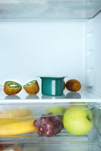 Plastic cup with yogurt and kiwi in refrigerator - Фото, изображение