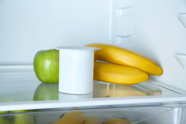Plastic cup with yogurt, bananas and apple in refrigerator - Photo, image