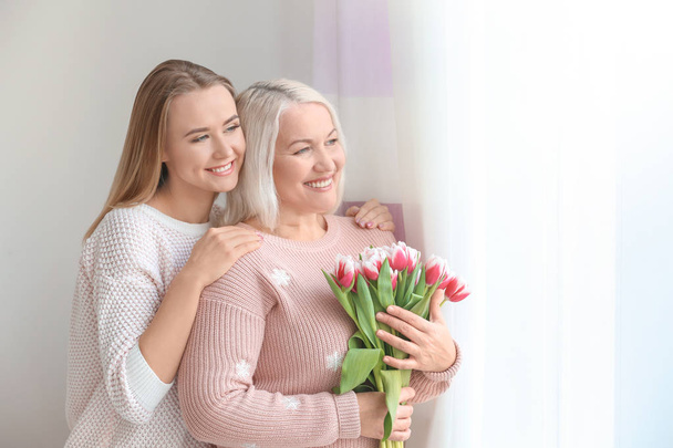 Young daughter and mother with bouquet of flowers at home - Photo, Image