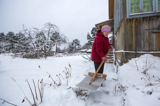 La donna anziana pulisce la neve vicino alla casa rurale
. - Foto, immagini