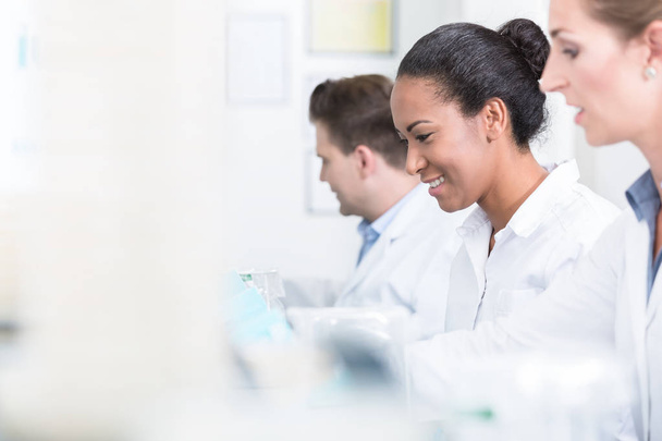 Группа исследователей улыбается во время работы над приборами в лаборатории
 - Фото, изображение