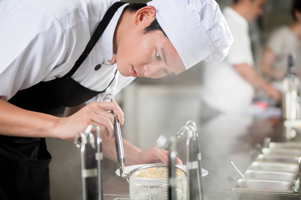 Jonge Aziatische chef-kok plating eten in restaurant zorgvuldig pipetting garnituur op de kant van de plaat - Foto, afbeelding