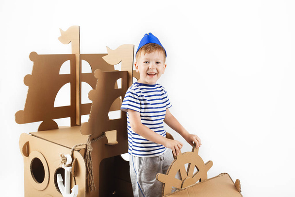 Kleine jongen spelen met kartonnen schip op witte achtergrond. Happ - Foto, afbeelding