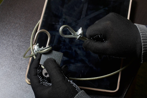 Computer security. Protection of access to data. The tablet is protected by a security cable and a lock. An attacker with gloves tries to open the lock and get access to the computer. - 写真・画像