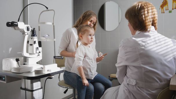 Ophthalmologist in clinic explains diagnosis about girls eyesight - child plays - Photo, Image