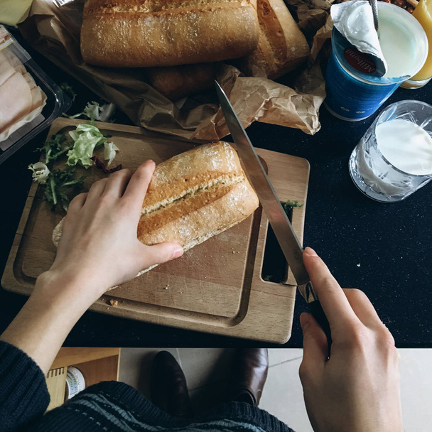 Ahşap doğrama tahtası üzerinde bıçakla kadın kesme ekmek görünümünü kırpılmış. - Fotoğraf, Görsel